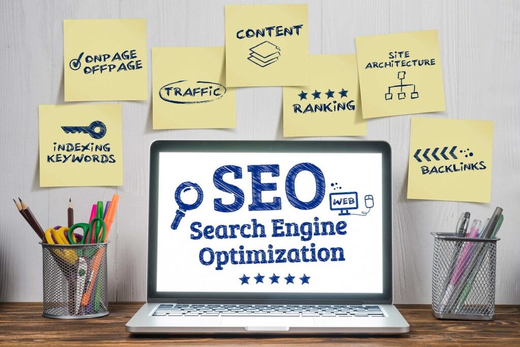 Laptop on a desk displaying 'SEO — Search Engine Optimization' with sticky notes about keywords, content, ranking, and backlinks.
